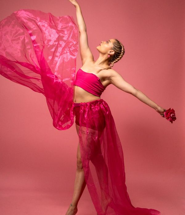 Woman performing a fluid cardio movement in a dark studio with pink light.